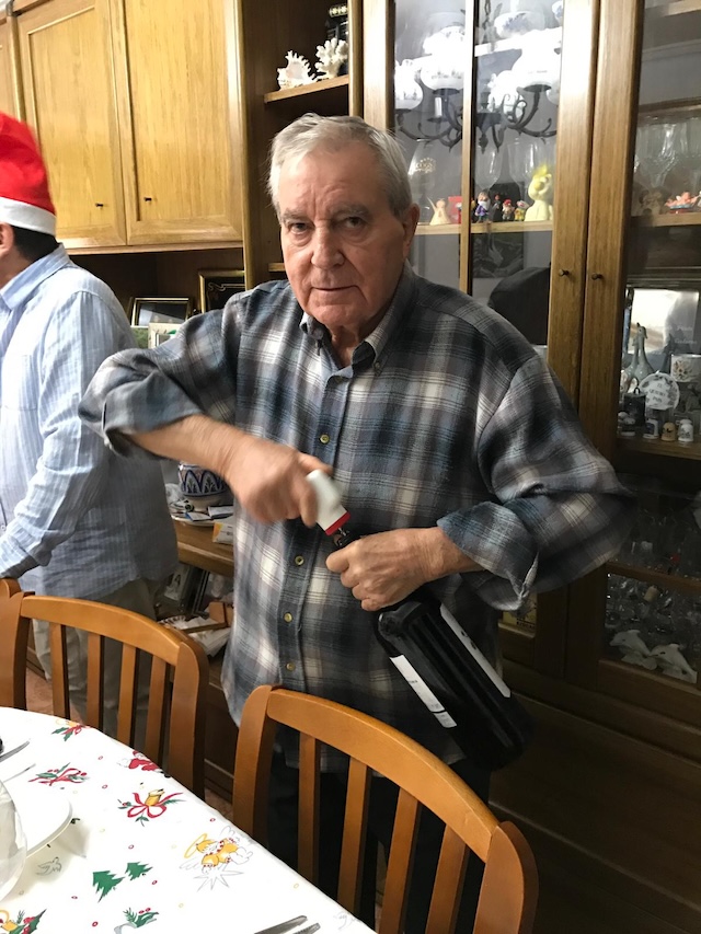 Hombre mayor abriendo una botella de vino en una comida familiar