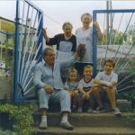 Familia reunida en una casa de pueblo, varias generaciones sentadas en la entrada con uvas recién cogidas