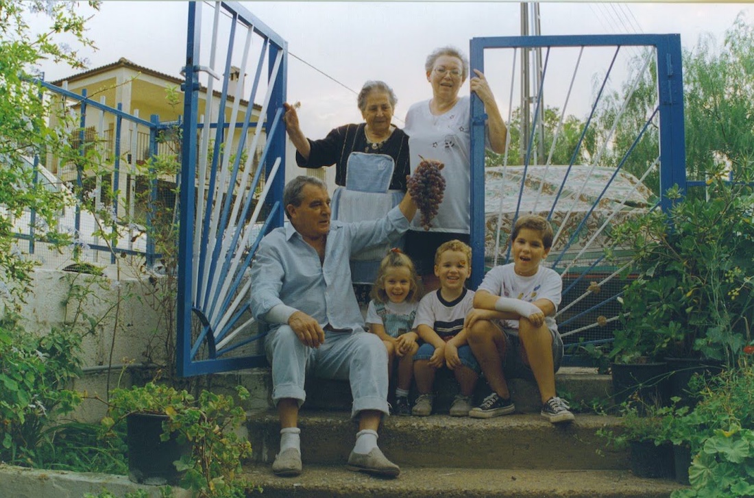 Familia reunida en una casa de pueblo, varias generaciones sentadas en la entrada con uvas recién cogidas