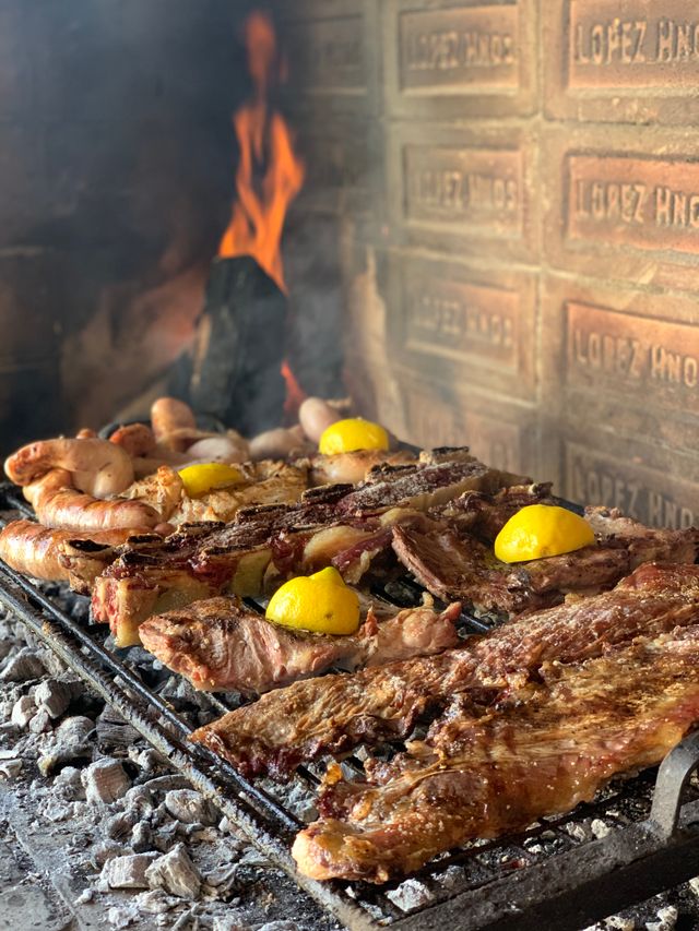 Asado argentino tradicional cocinándose sobre brasas con diferentes cortes de carne y chorizos.
