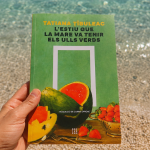 Libro L'estiu que la mare va tenir els ulls verds de Tatiana Tîbuleac sostenido frente al mar durante unas vacaciones de verano en Grecia