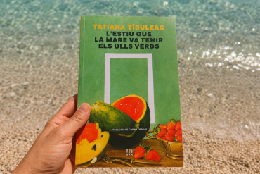 Libro L'estiu que la mare va tenir els ulls verds de Tatiana Tîbuleac sostenido frente al mar durante unas vacaciones de verano en Grecia