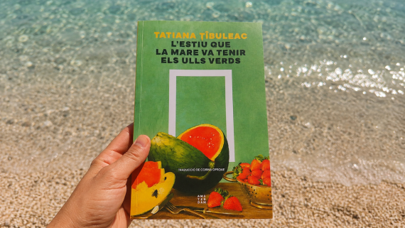 Libro L'estiu que la mare va tenir els ulls verds de Tatiana Tîbuleac sostenido frente al mar durante unas vacaciones de verano en Grecia