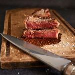 Chuletón de carne madurada cortado y servido sobre una tabla de madera con sal en escamas