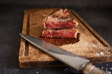 Chuletón de carne madurada cortado y servido sobre una tabla de madera con sal en escamas