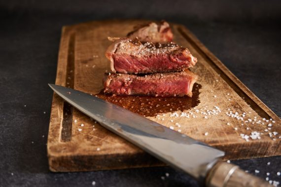 Chuletón de carne madurada cortado y servido sobre una tabla de madera con sal en escamas