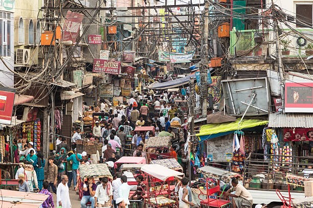 Calle concurrida en la India con comercios, peatones, rickshaws y numerosos cables sobre los edificios.