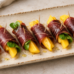 Rollos de cecina con mango en una fuente alargada, algunos con canónigos, aliñados con aceite de oliva y pimienta.
